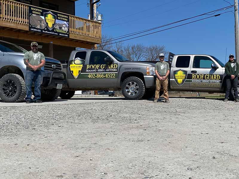 Roof Guard team members posing for a picture next to their work pickups in front of their main office