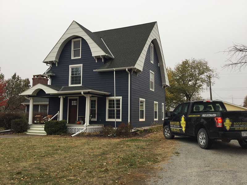 Small, two-story home with newly installed dark blue siding by Roof Guard