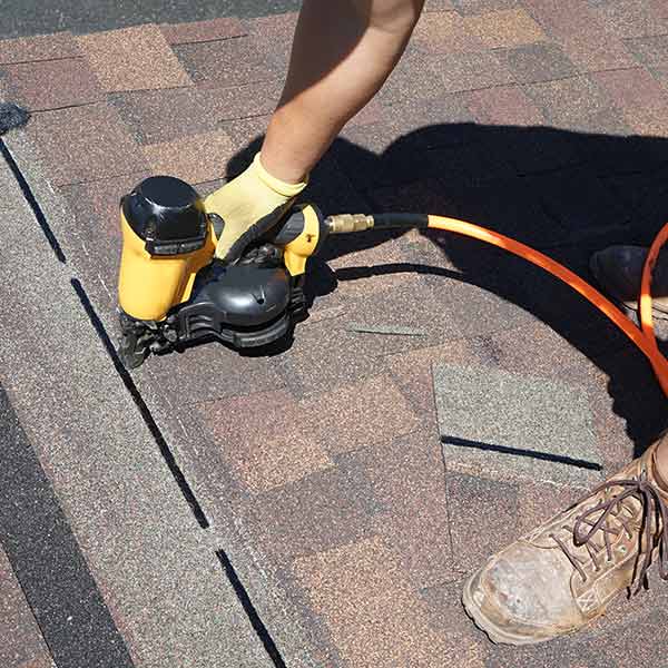 Close up of a worker installing new asphalt shingles on a residential roof with a nail gun